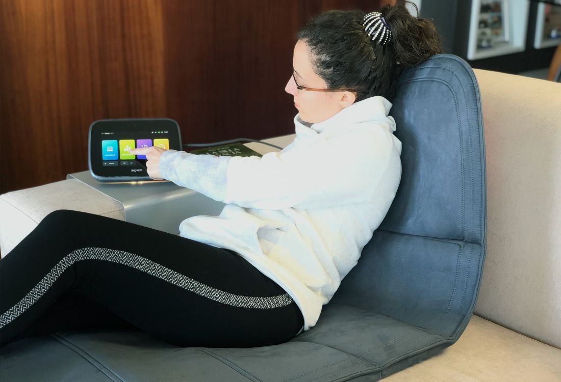 Mujer de 35 a 40 años aplicando la terapia Bemer con equipo B.Box EVO sentada en un sofá