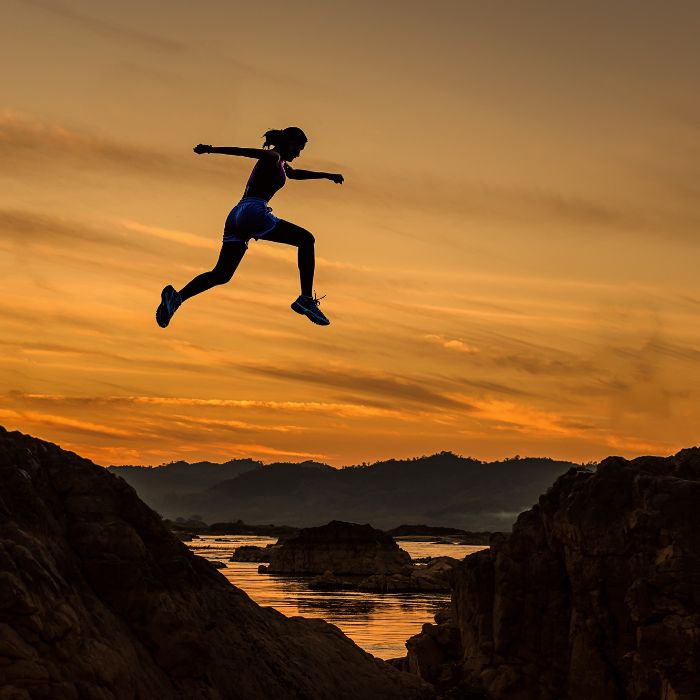 Mujer deportista saltando entre piedras en una playa mientras anochece