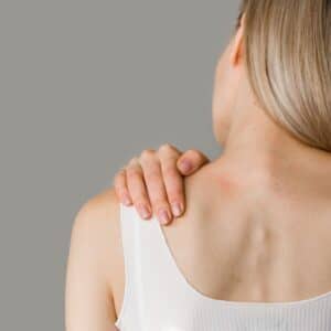 Mujer de espaldas tocándose el hombro izquierdo representando el concepto de dolor de la fibromialgia