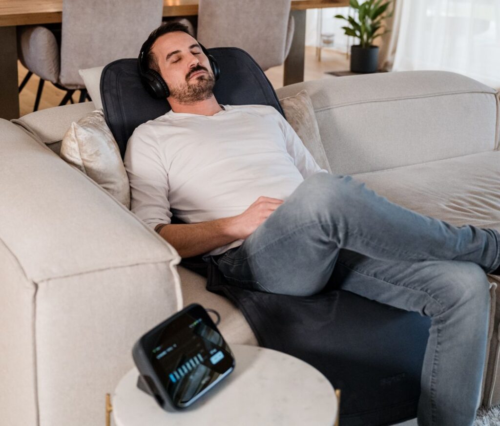 Hombre de mediana edad usando la terapia Bemer tumbado cómodamente sobre módulo de aplicación B.BODY EVO en el sofá de su casa