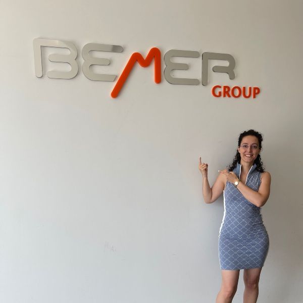 Noelia Otero señalando logo de BEMER detrás situado sobre pared blanca