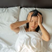 Mujer tumbada en la cama sufriendo dolor de cabeza debido al insomnio, falta de sueño
